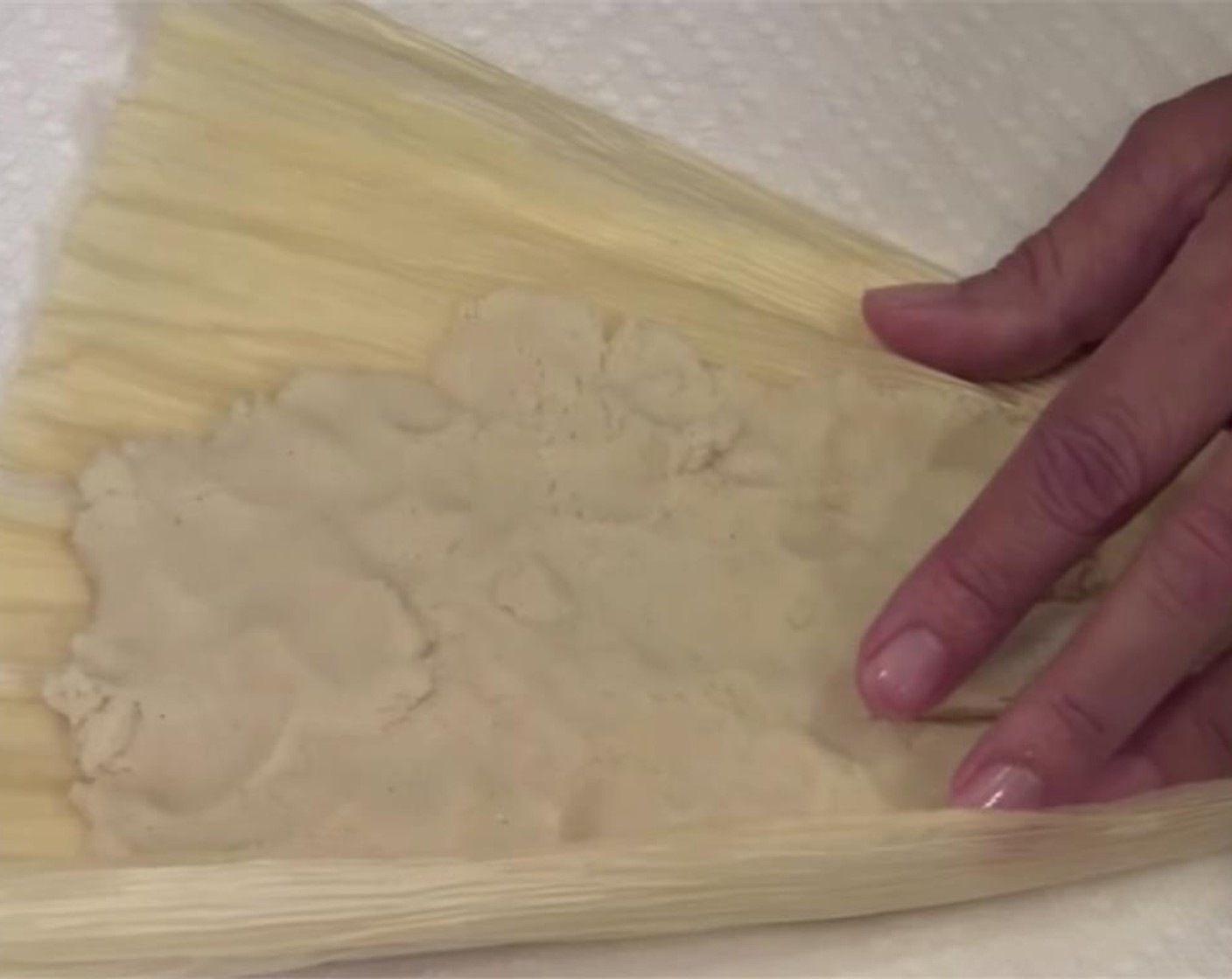 step 8 For assembly, take a few corn husks out of water, and pat dry with a paper towel. Spread a spoonful of masa on the corn husk, leaving the pointy end and a 1/2 inch margin on the other end bare.