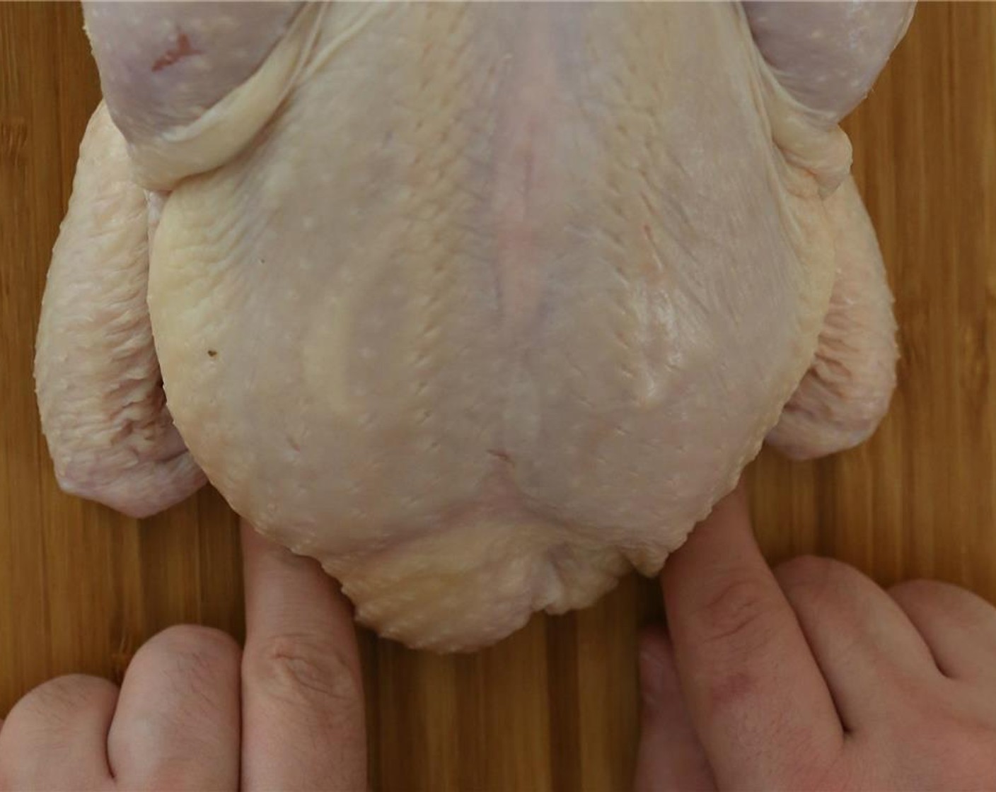 step 4 Keep your fingers on the butcher twine. Pull it down the cutting board and over the wings