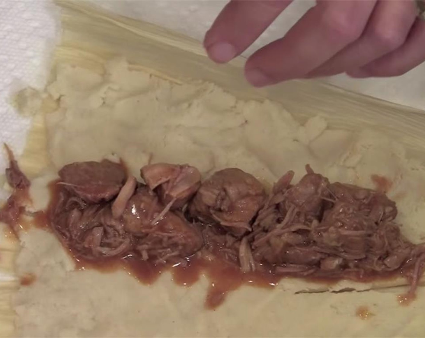 step 9 Place several chunks of pork down the center of the masa, then fold the masa over so that the ends meet. Roll, and fold up the end to encase the filling. Tie with a thin strip of corn husks. Place in the steamer, open end up, and repeat.
