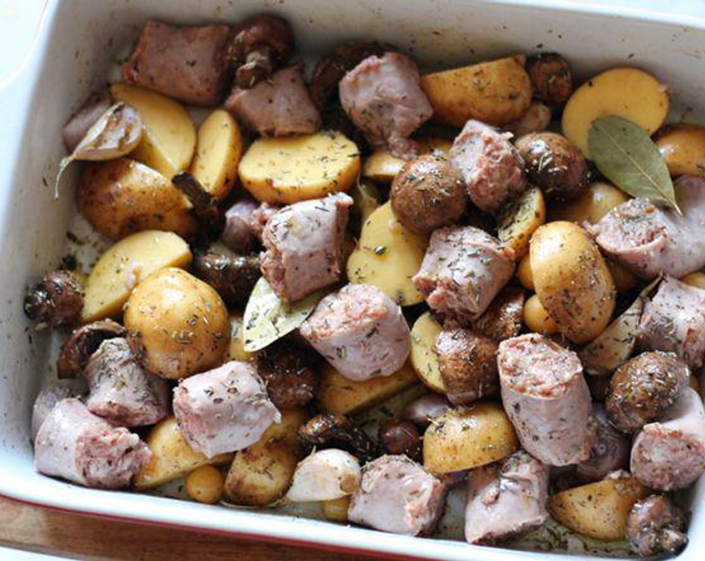 step 2 Mix Spicy Italian Sausage Link (1 lb), Yukon Gold Potatoes (6), Cremini Mushroom (1 cup), Tomatillo (1 cup), Garlic (1 handful), Shallots (2), Olive Oil (4 Tbsp), Bay Leaves (2), Dried Thyme (1 Tbsp), Dried Rosemary (1 Tbsp), and Balsamic Vinegar (1 Tbsp) together in a baking pan coating everything evenly.