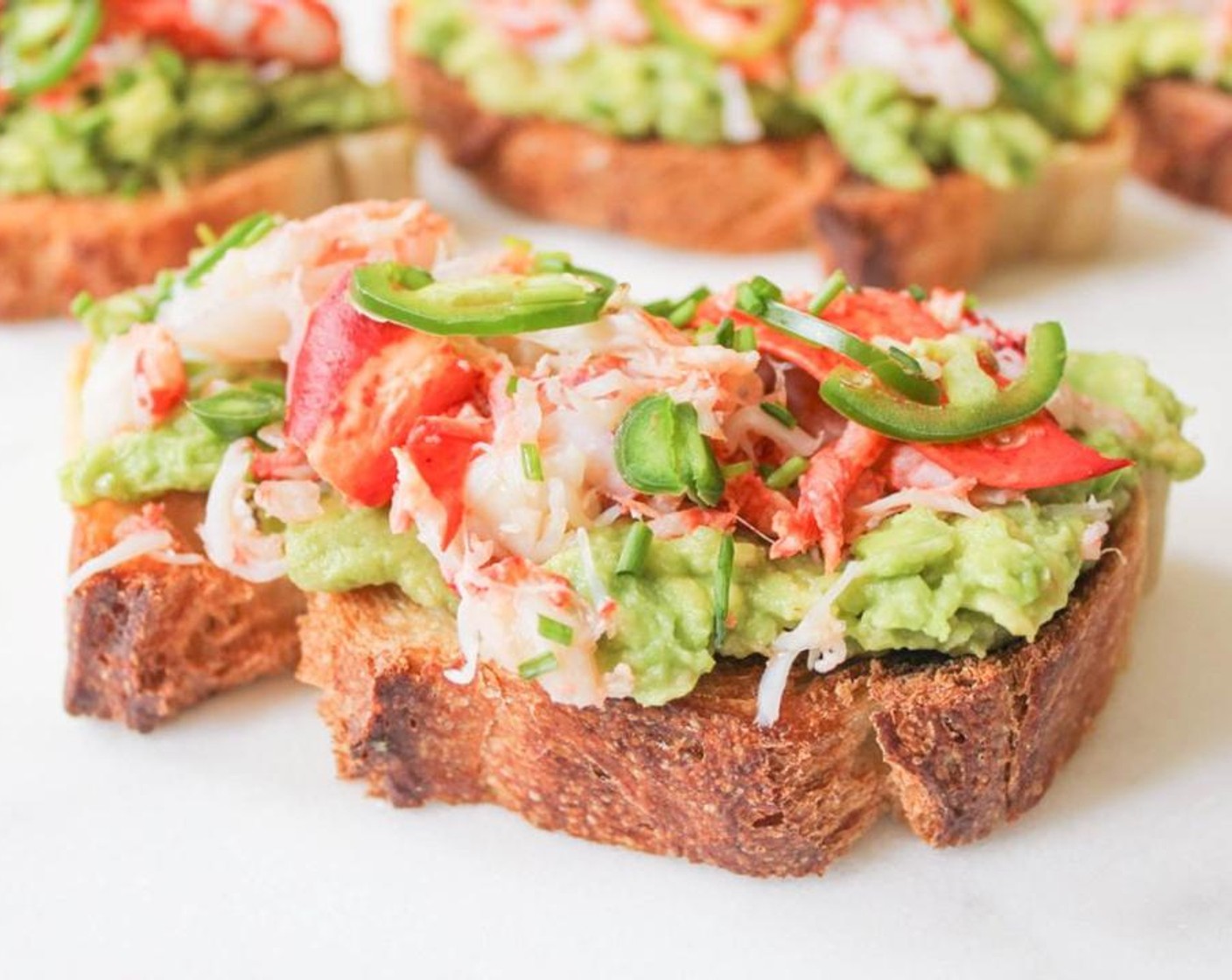 step 6 Spread each piece of toast with a thick layer of avocado mash. Top with the chopped lobster meat, then sprinkle with Jalapeño Pepper (1) and Fresh Chives (2 tsp). Drizzle each with a little bit of Extra-Virgin Olive Oil (to taste).