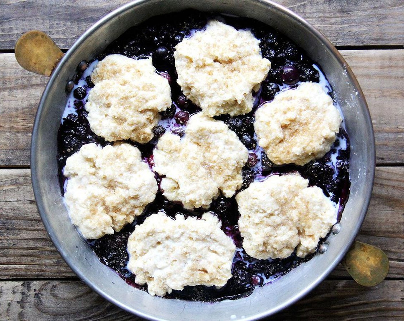 step 6 To assemble and bake the cobbler: Remove the berries from the oven; increase the oven temperature to 425 degrees F (220 degrees C). Drop the pieces of biscuit dough on the hot berry filling, spacing them about half inch apart. Brush biscuits with Milk (2 tsp) and sprinkle with Raw Cane Sugar (2 tsp).
