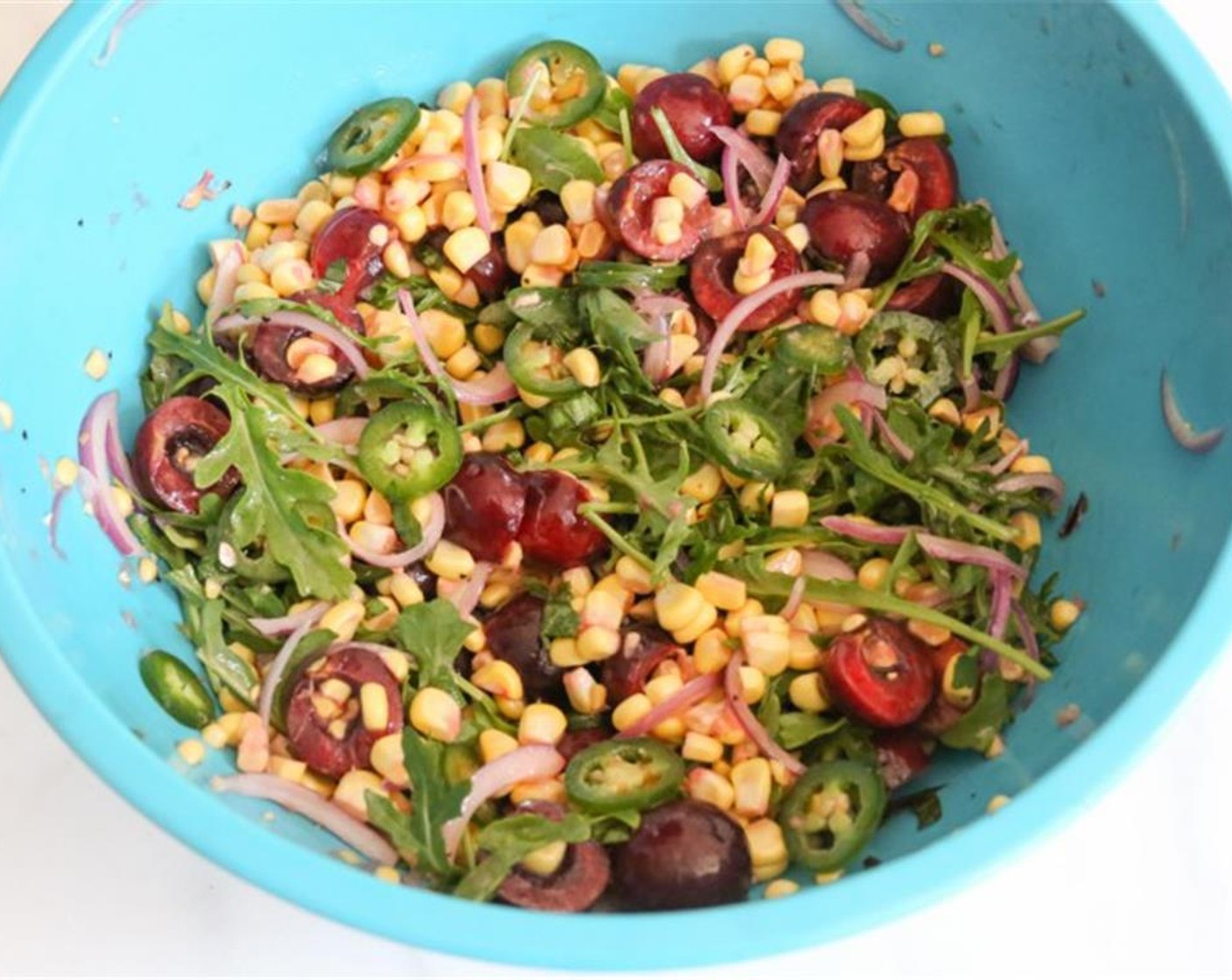 step 4 Carefully slice the kernels from each ear of Sweet Corn (2 ears) into a large mixing bowl. Add the Sweet Cherries (2 cups), very thinly sliced Red Onions (4 Tbsp), Jalapeño Pepper (1), Baby Arugula (1 cup) and Fresh Basil Leaves (8) to the bowl and toss to combine.