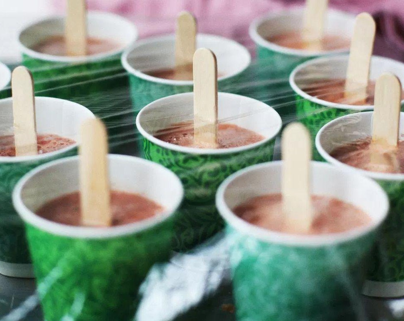 step 3 Pour mixture into Dixie cups, and place on a baking sheet. Cover with plastic wrap and cut holes on top to insert the popsicle sticks so that they stand up straight.