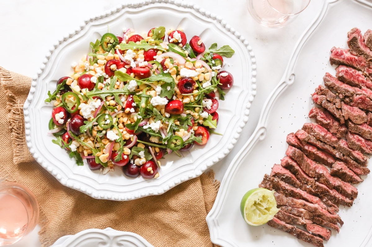 Marinated steak with a sweet corn and cherry salad featuring arugula, feta, red onion, and jalapeños.